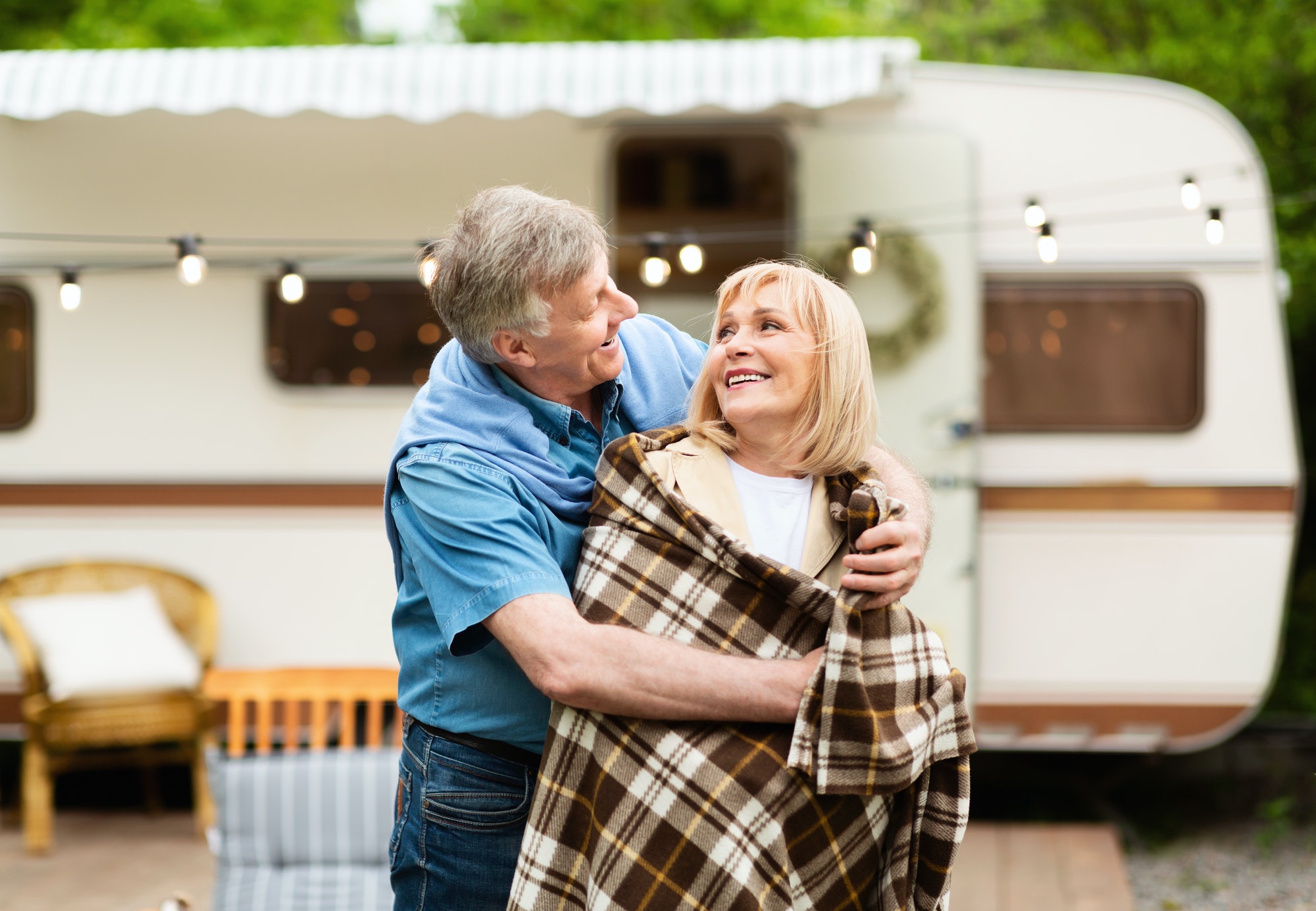 Caring senior man covering his beloved woman with blanket near motorhome at camping site