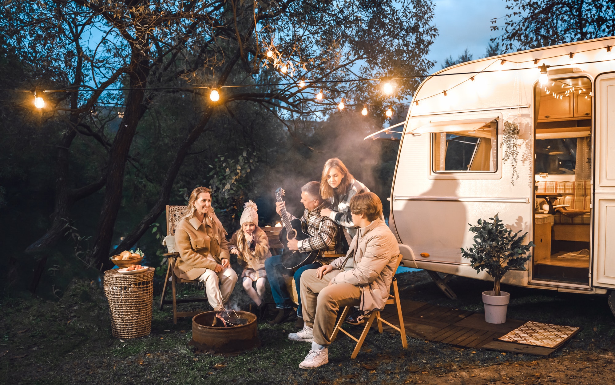 Family trailer travel.Children,brother sister,mom dad playing guitar,singing song at fire.Evening