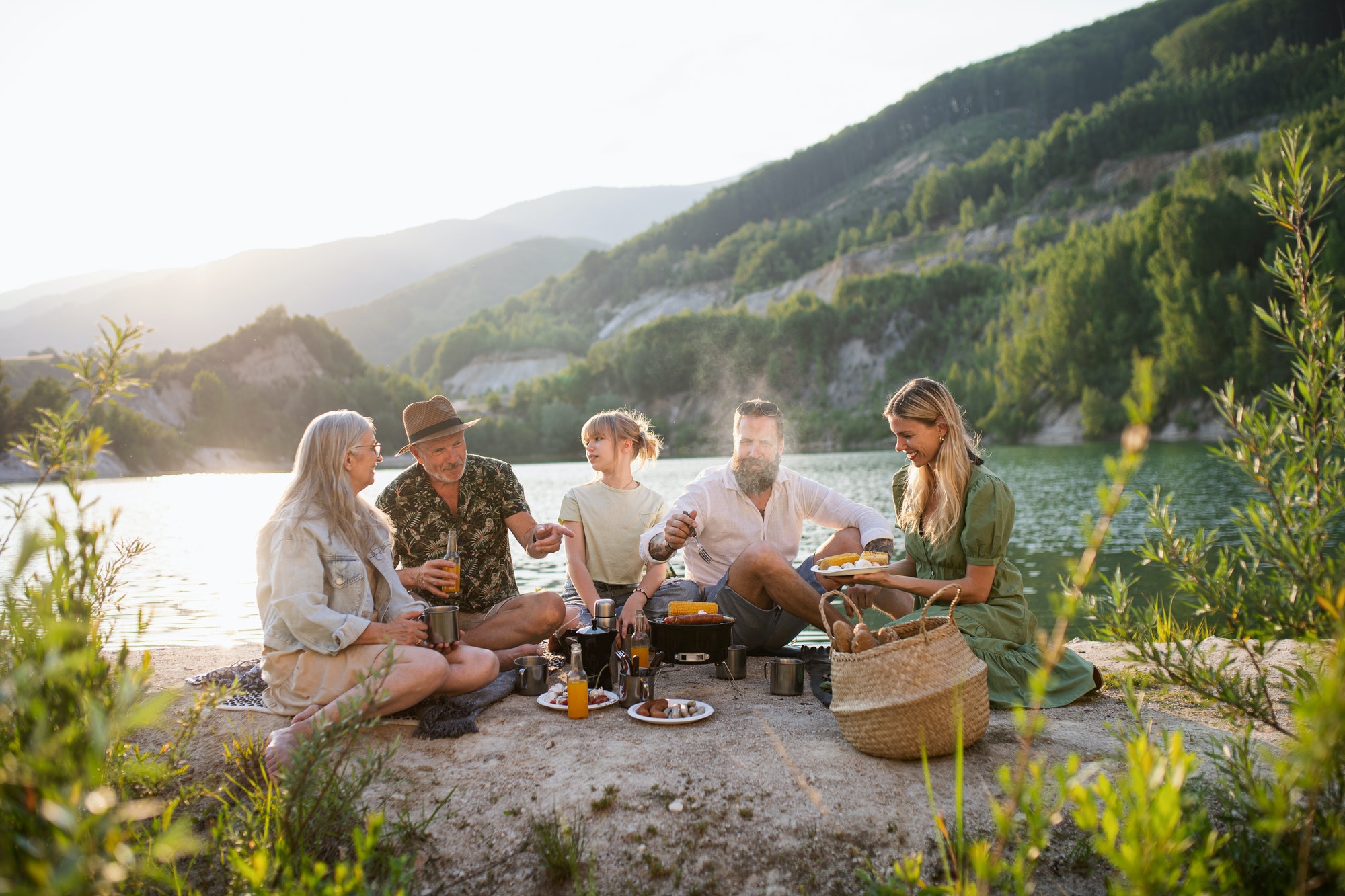 Happy multigeneration family on summer holiday trip, barbecue by lake