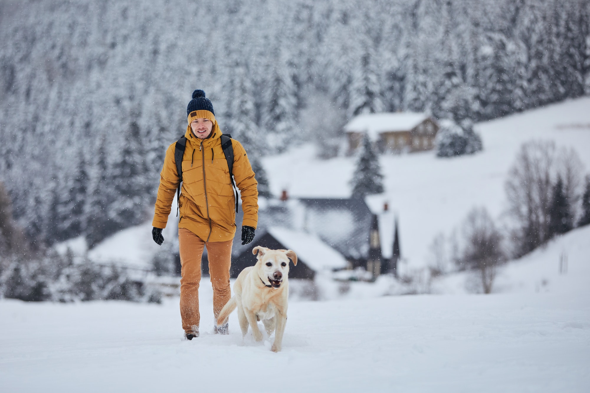 Man with dog walking in snow against old village in beautiful nature