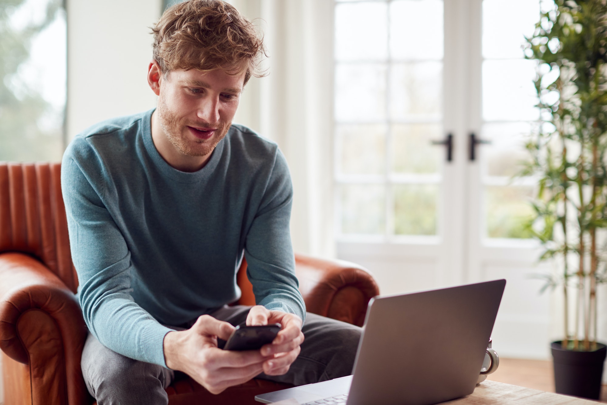 Man Working From Home Using Laptop And Mobile Phone