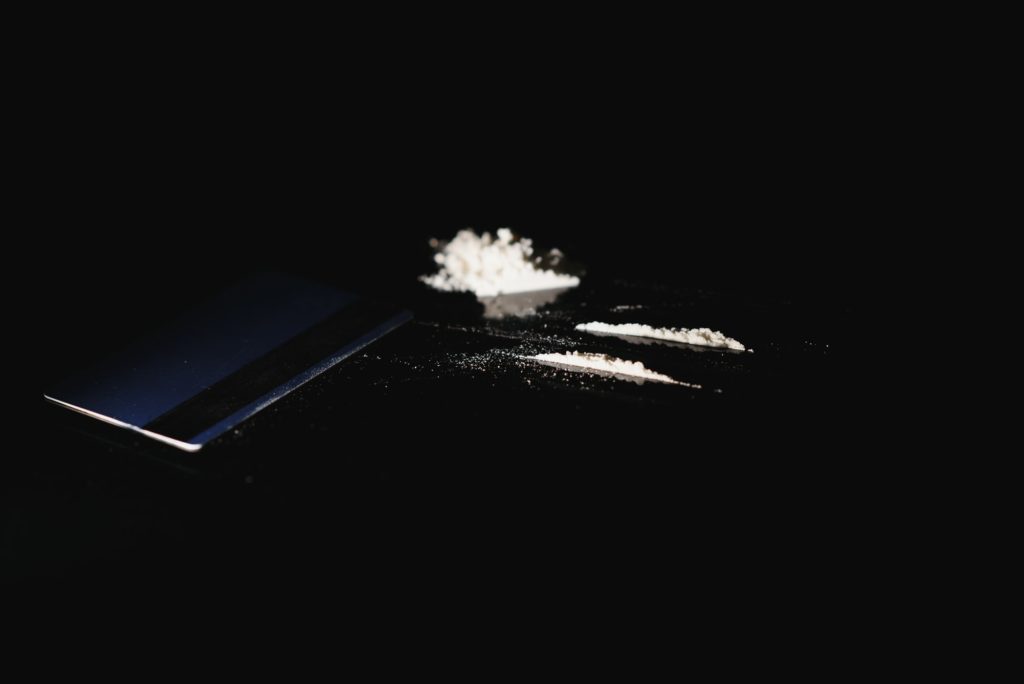 Close up of hands of young druggie is doing tracks of cocaine with a credit card.