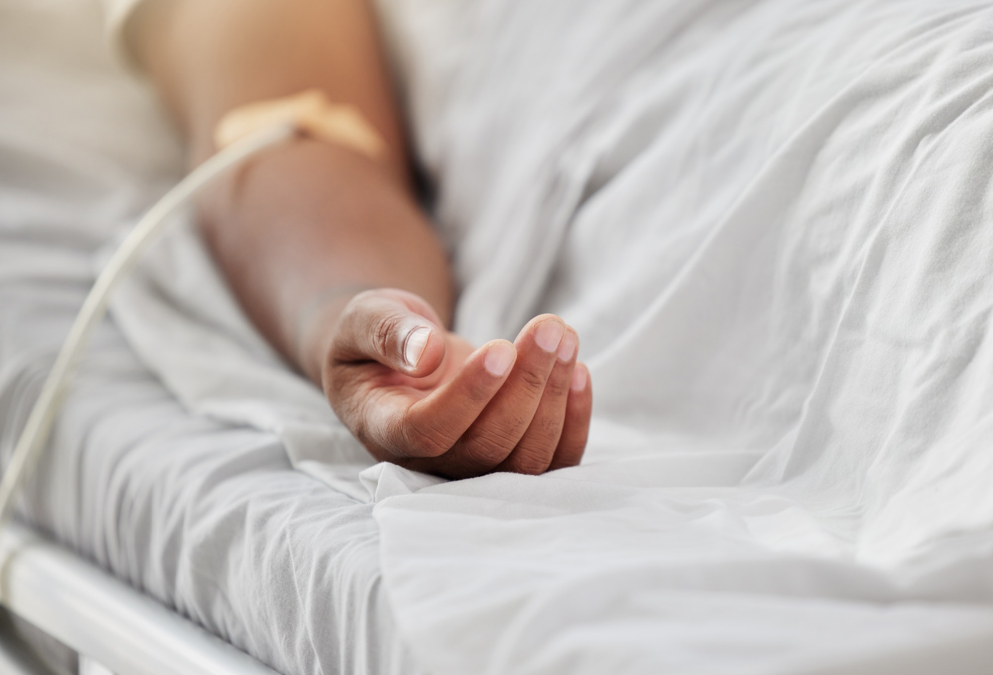 Closeup shot of the hand of an african american man lying in a hospital bed inside of a ward. Mixed