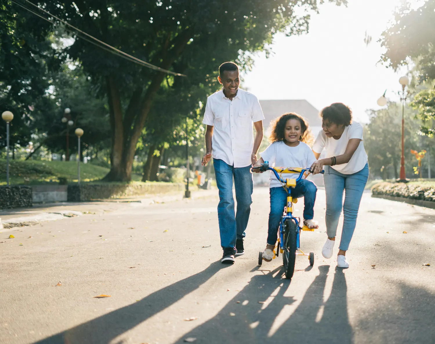 mom and dad teaching child to ride a bike